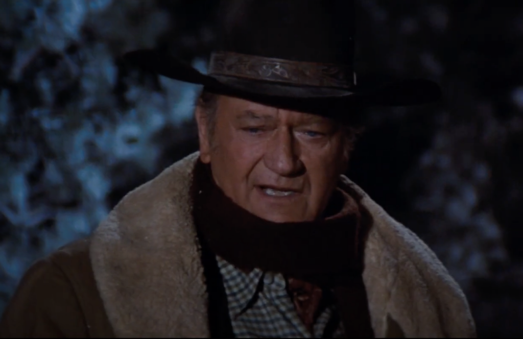 A still and close-up image of John Wayne on a horse at nighttime. 