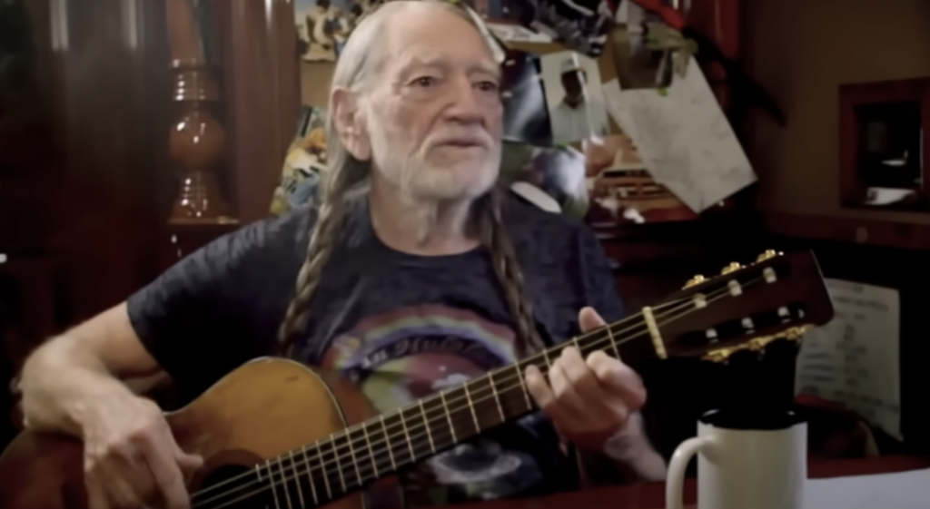 A still image of Willie Nelson playing the guitar. 