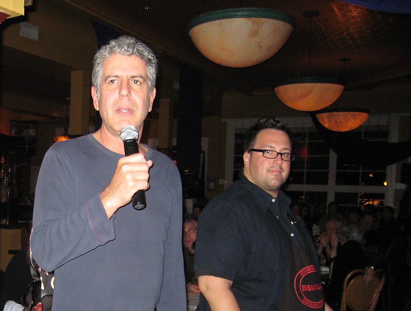 An image of Anthony Bourdain giving a speech with a microphone. 