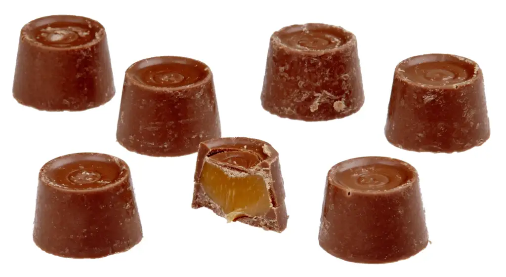 Seven round Rolo chocolates, six whole and one cut in half, revealing a caramel filling inside. The chocolates are arranged in a casual pattern on a white background.