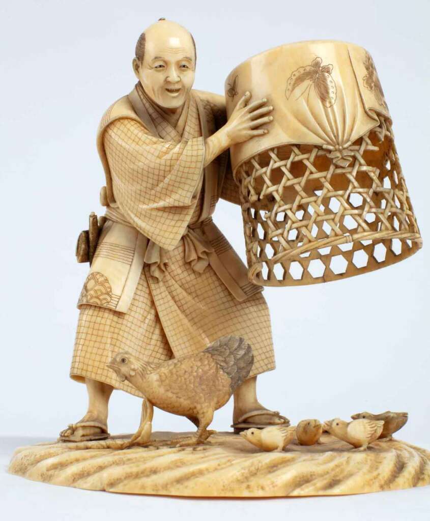 An intricate wooden sculpture depicts a man in traditional Japanese attire, lifting a detailed woven basket. Below him, a hen and several chicks are carved with fine details, standing on a textured base. The artwork showcases meticulous craftsmanship.