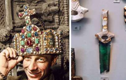 A man wearing a richly decorated, gem-studded crown adorned with various colored stones and a cross poses near an exhibit. Beside him, a display showcases an ornate ceremonial dagger with a green blade and jeweled hilt, accompanied by several numbered artifacts.