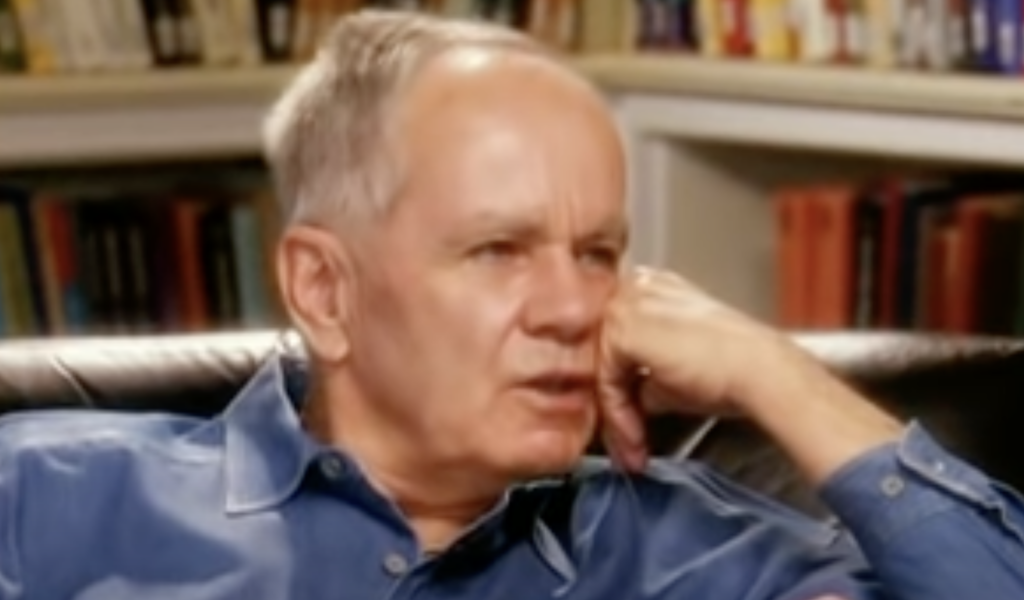 Cormac McCarthy resting his face in his hand while wearing a blue shirt. 