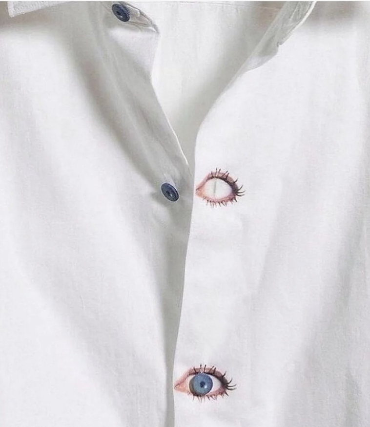 A very creepy looking white button down shirt with eyes next to each button.