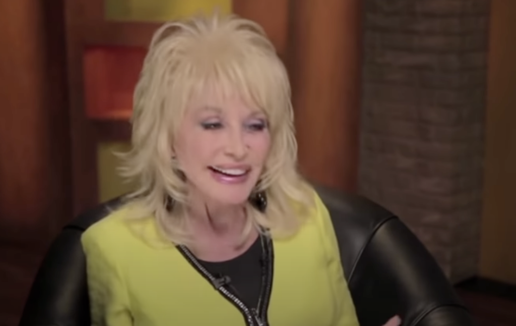 Dolly Parton laughing while being interviewed in olive green shirt. 
