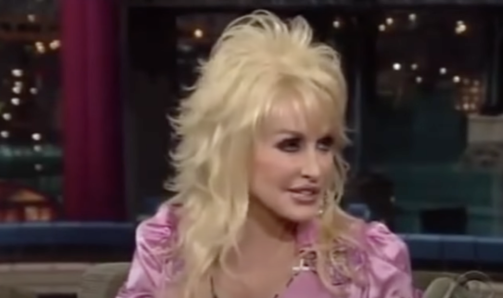 Dolly Parton being interviewed in a pink shirt. 