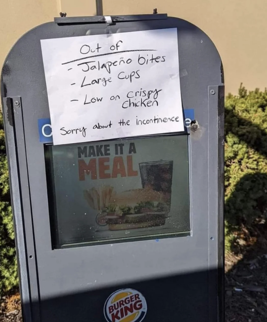 A Burger King drive-thru menu sign has a handwritten note taped to it. The note reads: "Out of Jalapeño bites, Large Cups, Low on crispy Chicken. Sorry about the incontinence." The Burger King logo is visible at the bottom of the sign.