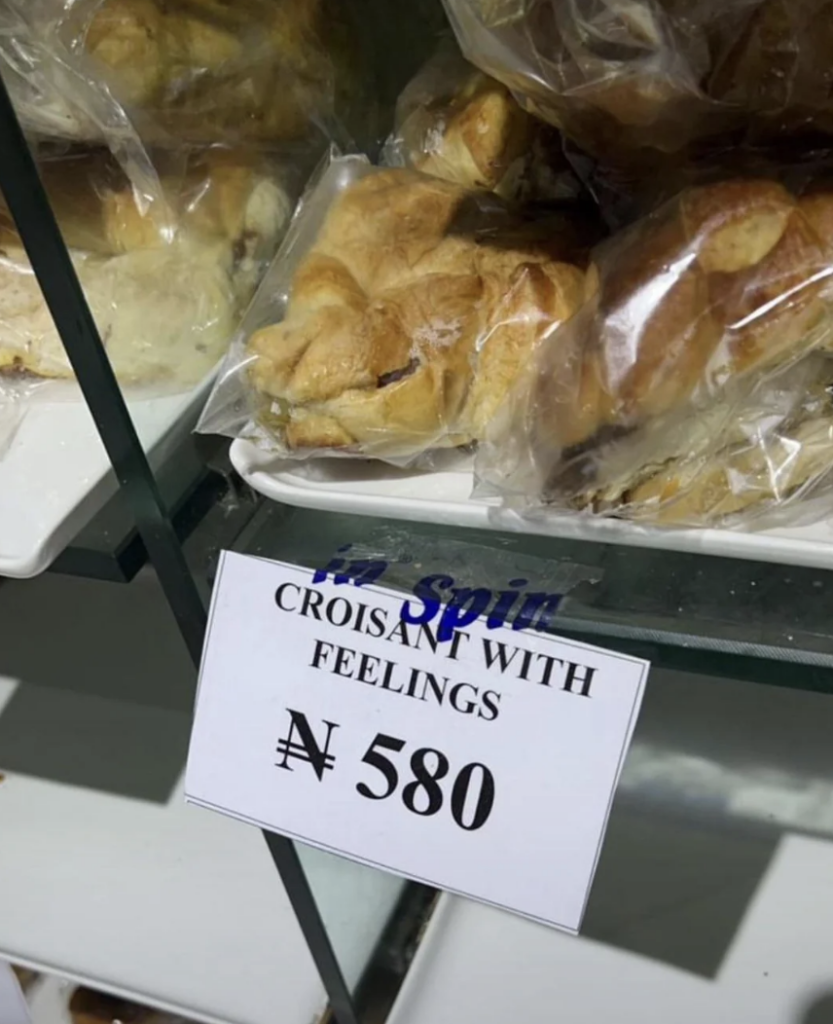 A display shelf showcases several packaged croissants behind a glass, with a price tag reading "Croissant with Feelings" priced at ₦580. The croissants are in clear plastic wraps and placed on white ceramic plates.