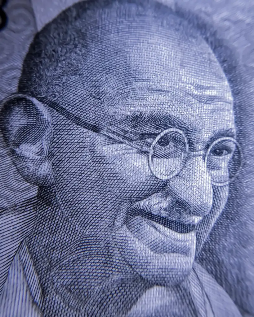 Close-up image of an intricate portrait of an elderly man with round glasses, a mustache, and a bald head with short hair on the sides. The detailed texture and lines give a lifelike quality, suggesting that the image is likely taken from a banknote.