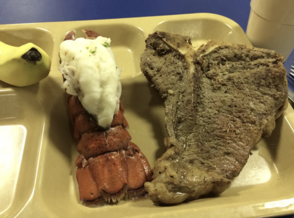 An image of a giant piece of steak next to a giant lobster on a dinner tray. 