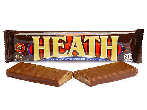 A Heath milk chocolate English toffee candy bar is partially unwrapped, revealing its packaging with bold red and yellow letters. In front of the wrapper lies the chocolate bar, broken in half, showing its toffee interior. The packaging notes it's 1.4 oz and 210 calories.