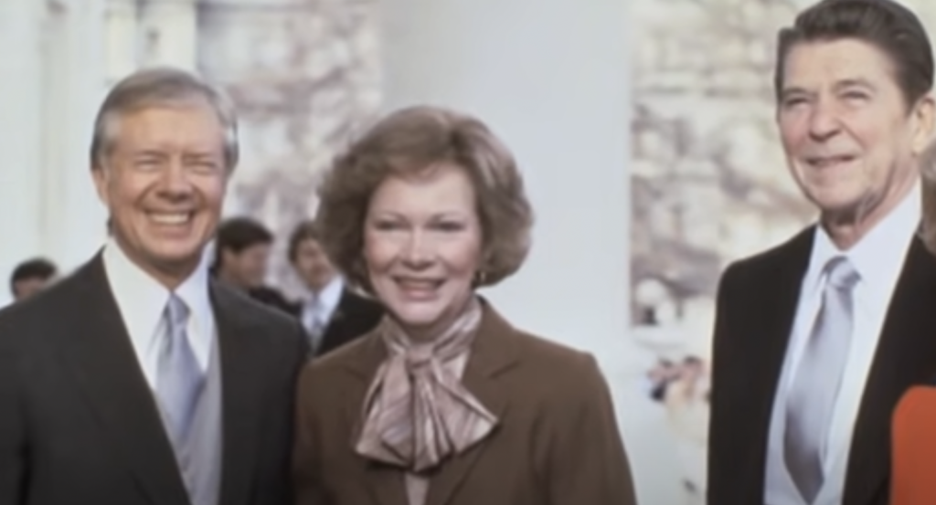 Three individuals, two men and one woman, stand closely together, smiling warmly. The man on the left and the woman are dressed in formal attire, with the man wearing a suit and tie. The man on the right is also in a suit. They are outdoors with trees in the background, embodying the essence of Jimmy Carter quotes about unity.