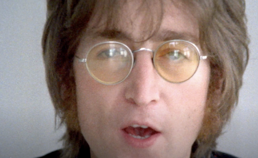 An image of John Lennon in sunglasses looking at the camera. 