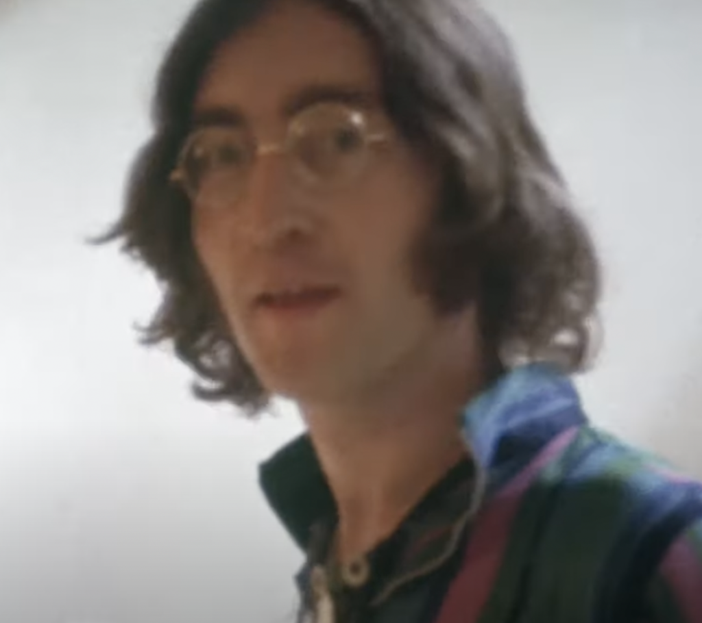 A close-up image of John Lennon looking at the camera with sunglasses on. 