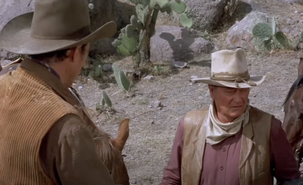 A still image of John Wayne talking seriously. 