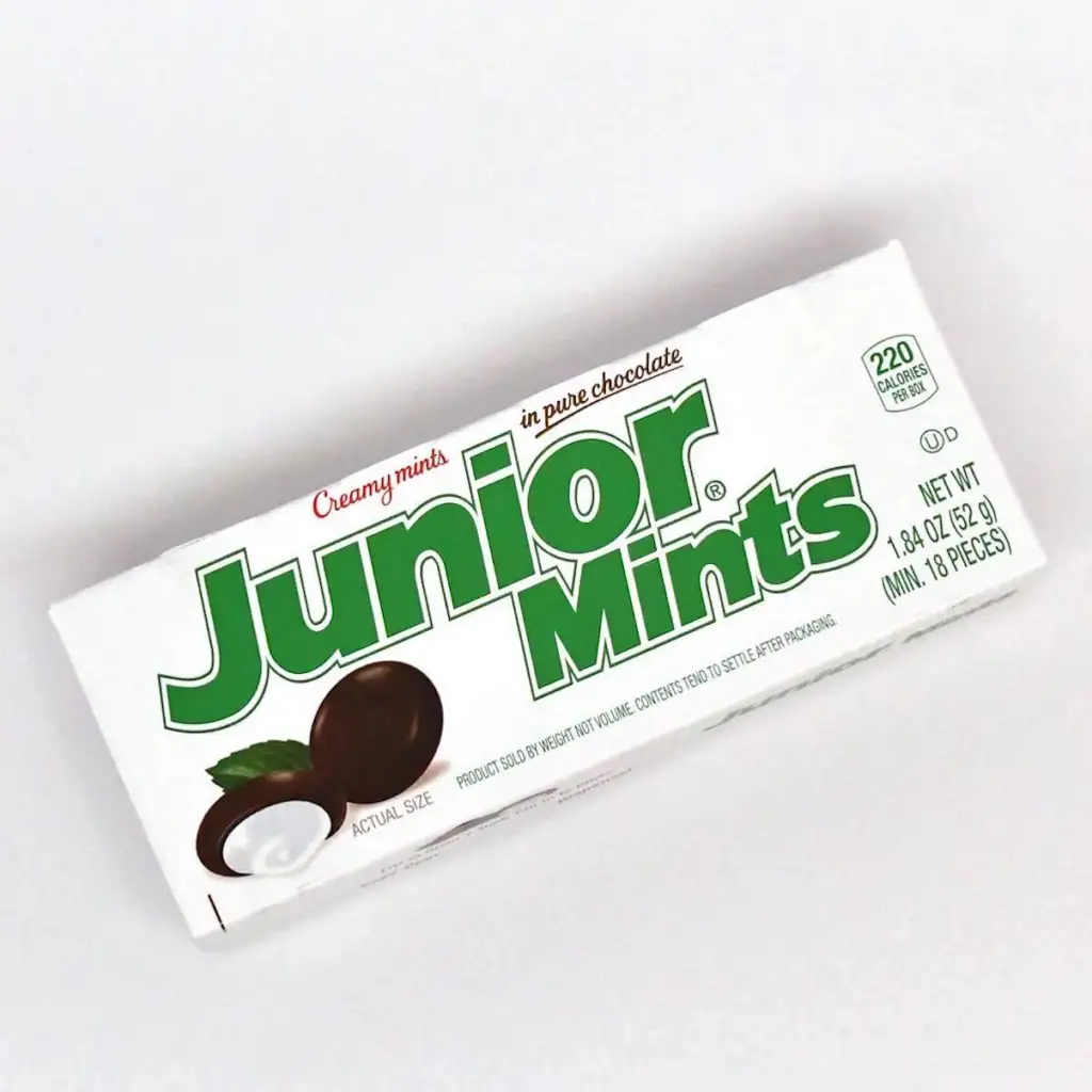 A white rectangular box of Junior Mints candy, featuring the brand's name in large, green letters with brown and white mints pictured on the front. The text "Creamy mints in pure chocolate" and "NET WT 1.84 OZ (52.1g)" are also visible.