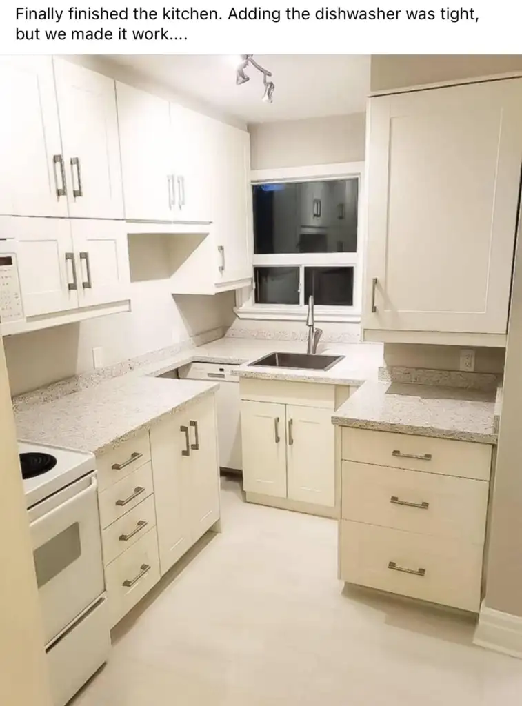 A small, modern kitchen with white cabinets, a stainless steel sink, and a dishwasher integrated into the cabinetry. The countertops are light-colored, and there's a window above the sink. The floor is light-colored, complementing the overall bright aesthetic.