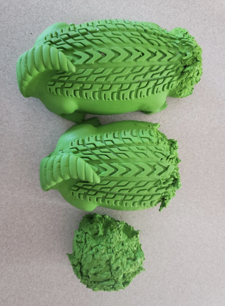 Three green pieces of playdough sit in a vertical line against a light gray background: the top two pieces are textured with intricate patterns, resembling tire treads or leaf veins, while the bottom one is roughly spherical with an uneven, coarse surface.