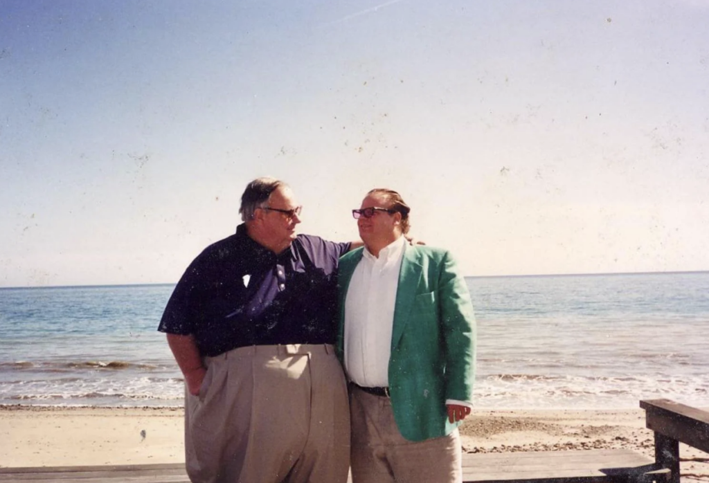 An image of Chris Farley with his dad in front of a beach. 
