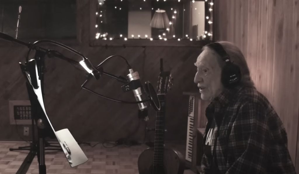 An image of Willie Nelson singing in studio. 