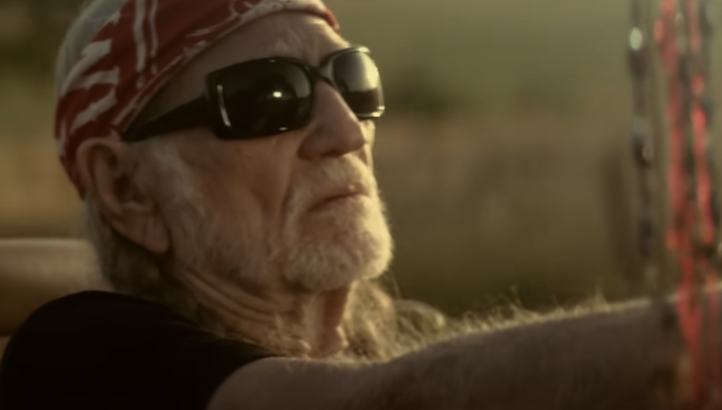 A still image of Willie Nelson driving. 