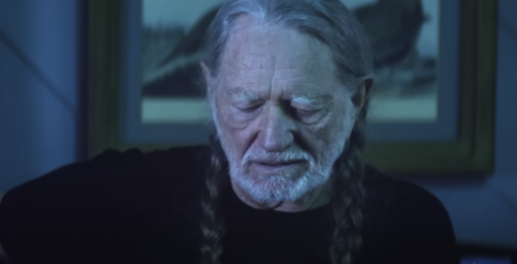 A still image of Willie Nelson looking down. 