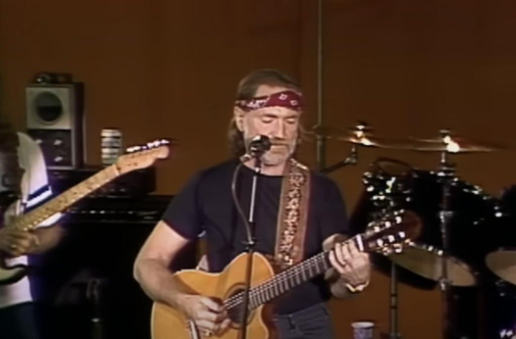 A still image of Willie Nelson playing a live show. 
