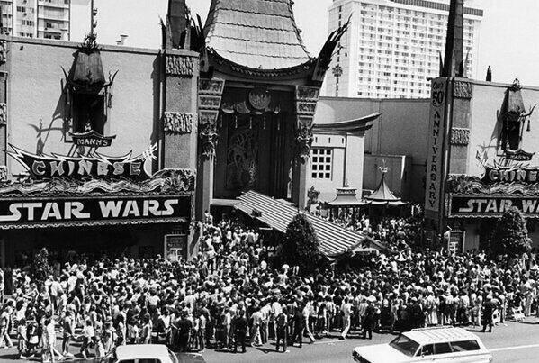 A large crowd gathers outside Grauman's Chinese Theatre for the premiere of a "Star Wars" movie. The iconic theater marquee, featuring the film's title, is prominently displayed. The street is bustling with people excitedly awaiting entry.