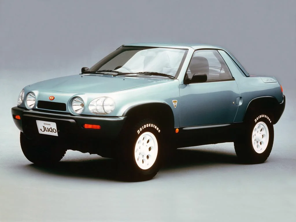 A light blue Isuzu Judo concept car with a compact, sporty design is shown against a plain background. The car has a unique front grille with dual round headlights, white wheels, and a rugged stance suitable for off-road driving.