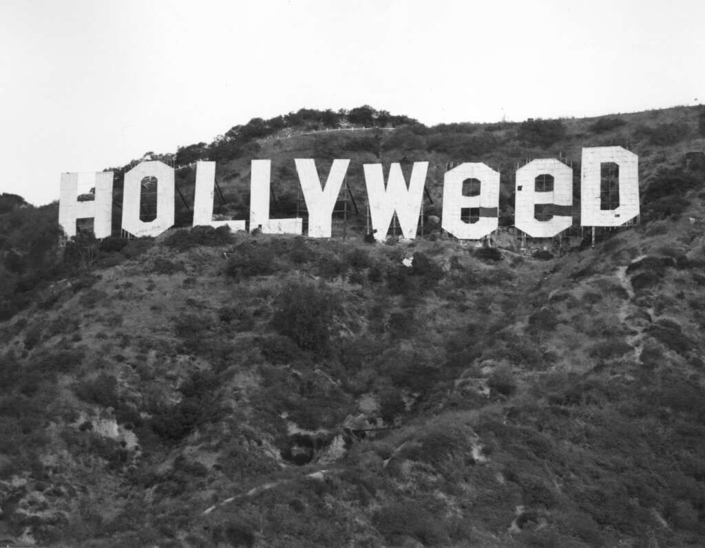 Black-and-white photo of the Hollywood sign edited to read "Hollyweed." The letters are positioned on a hillside with foliage visible below, and the change to the text was done by altering the "O"s to resemble "E"s.