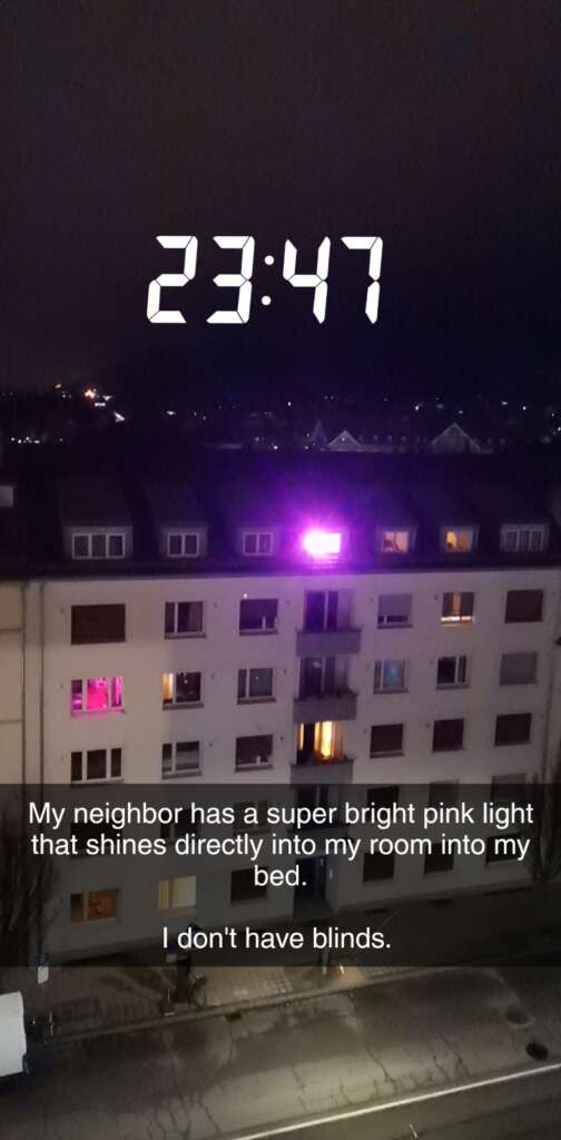 A nighttime view of an apartment building with a bright pink light shining from one of the windows. Text overlay reads, "My neighbor has a super bright pink light that shines directly into my room into my bed. I don't have blinds." The time displayed is 23:47.