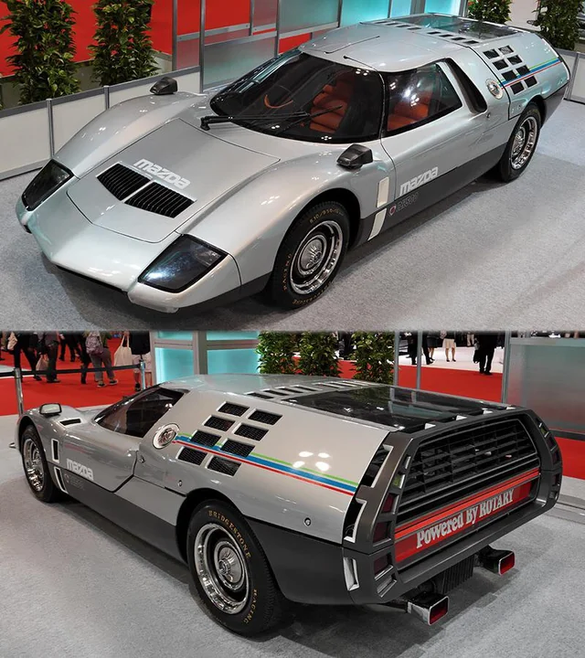 A silver Mazda RX500 concept car is displayed indoors. The sleek, futuristic design features distinctive black grills on the rear with "Powered by Rotary" text. The car is showcased from both front and rear angles, emphasizing its aerodynamic structure.