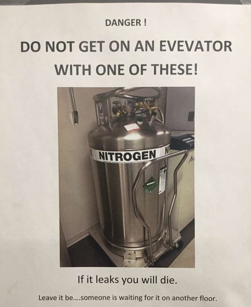 Sign warning about the dangers of riding an elevator with a nitrogen tank. It shows a cylindrical nitrogen tank in an elevator with the text: "DANGER! DO NOT GET ON AN ELEVATOR WITH ONE OF THESE! If it leaks you will die. Leave it be...someone is waiting for it on another floor.