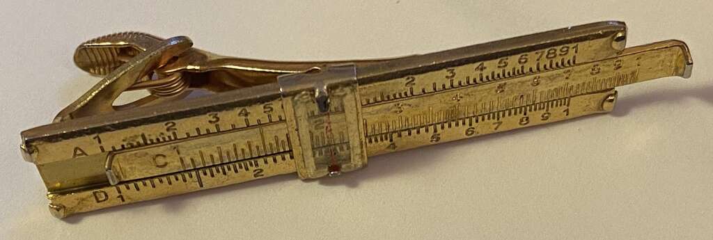 A small metal contraption resembling a combination of a clamp and a ruler. The top part appears to have a screw mechanism, while the bottom part has ruler markings. The device is gold-colored and has engraved scales labeled with "A," "C," and "D.
