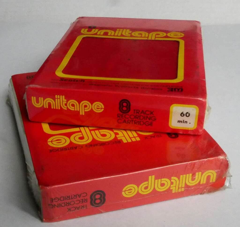 Two red Unitape 8-track recording cartridges are stacked on top of each other. The top cartridge has a sticker indicating "60 min." Both are encased in plastic wrapping. The Unitape logo and text are prominently displayed in yellow.