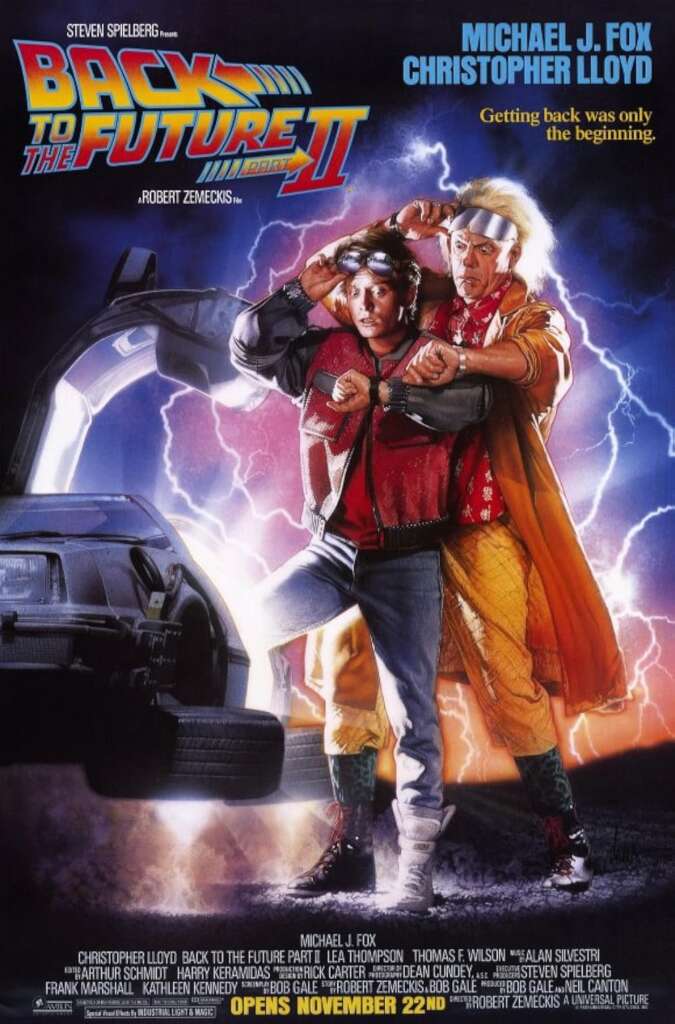 Poster of "Back to the Future Part II" featuring Michael J. Fox and Christopher Lloyd. They stand in front of a DeLorean time machine with the car's gull-wing door open. Both characters look surprised. The movie title and credits are displayed at the top and bottom.