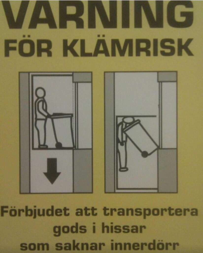 A yellow warning sign with black text and images. The top reads "VARING FÖR KLÄMRISK." Below are two diagrams: one with a person correctly moving a cart into an elevator, and another with the person being crushed by the cart. Text below warns against transporting goods in elevators without inner doors.