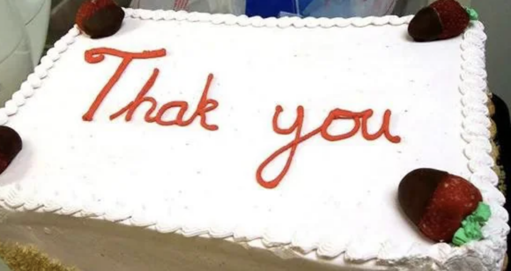 A rectangular cake with white frosting features the words "Thak you" written in red icing, missing the letter 'n' in 'Thank.' Each corner of the cake has a chocolate-covered strawberry as decoration.