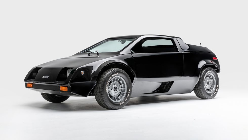 A sleek, black 1982 Urbacar Puma GT S2 stands on a plain white background. The car features a futuristic, angular design with a low-profile body, aerodynamic curves, and a sporty stance. It has large, stylish wheels and a compact, two-door configuration.