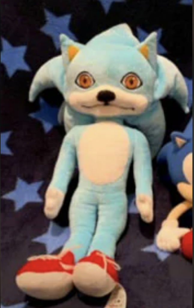 A plush toy designed to look like a blue anthropomorphic hedgehog with wide, orange eyes and a white belly. The toy has red shoes and is set against a dark background with blue stars.