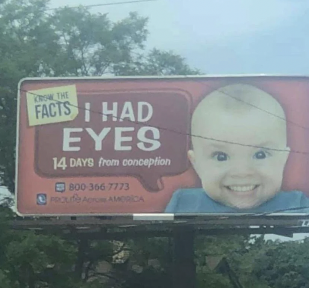 A billboard shows a smiling baby with text that reads, "KNOW THE FACTS: I HAD EYES 14 DAYS from conception." The billboard includes a phone number, 800-366-7773, and the logo for ProLife Across AMERICA on a red background. Trees are visible in the background.