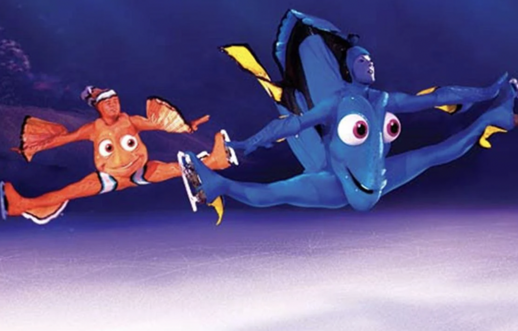 Two ice skaters are performing a split jump on an ice rink. They are dressed in elaborate costumes resembling characters from the animated film "Finding Nemo": one as Nemo, an orange clownfish, and the other as Dory, a blue tang fish.