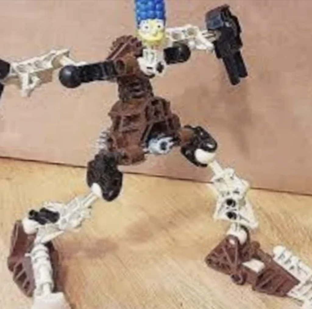 A LEGO creation featuring Marge Simpson's head on a robotic, skeletal body made from brown and white LEGO pieces. The figure is holding a small black object in one of its outstretched arms, standing on a wooden surface against a plain background.