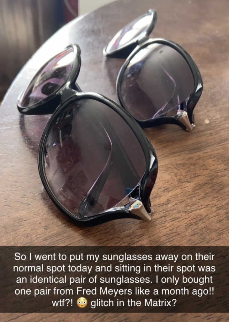 Two pairs of identical black sunglasses are placed on a wooden table. A caption below them reads: "So I went to put my sunglasses away on their normal spot today and sitting in their spot was an identical pair of sunglasses. I only bought one pair from Fred Meyers like a month ago!! wtf?! 😲 glitch in the Matrix?