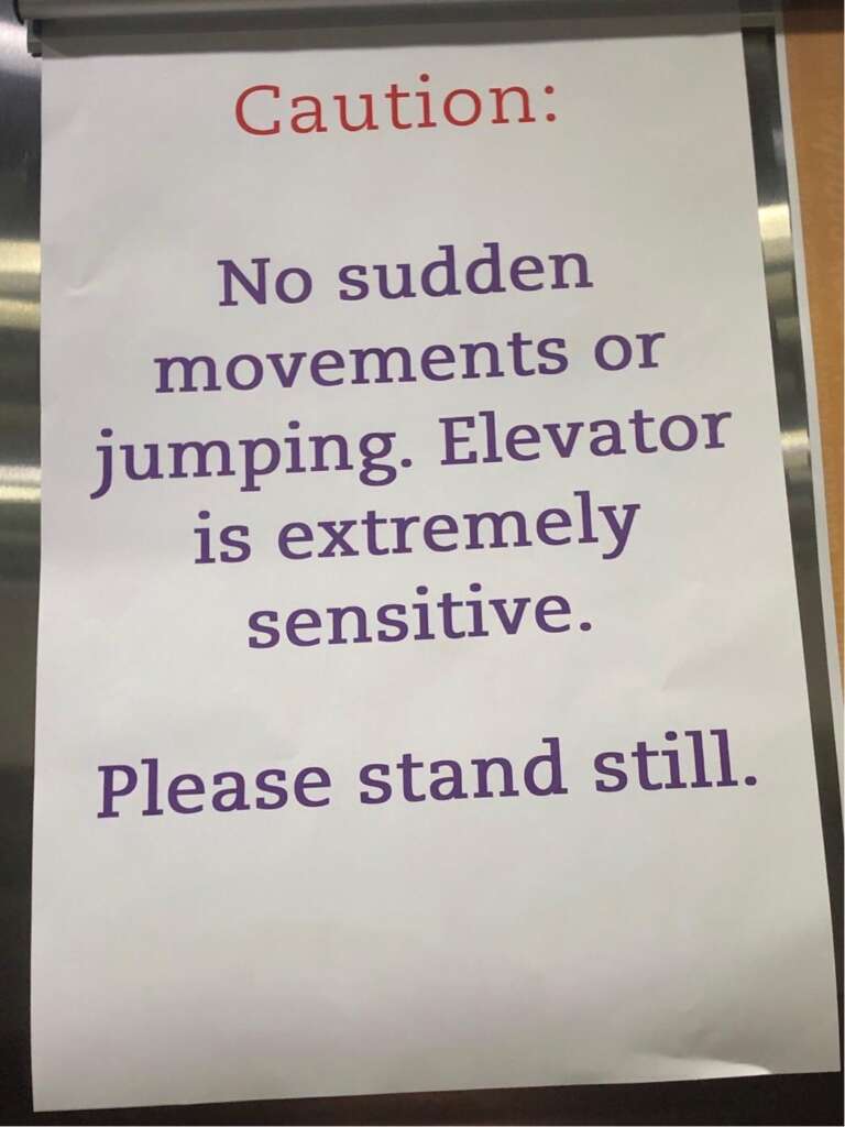 A sign on an elevator door reads: "Caution: No sudden movements or jumping. Elevator is extremely sensitive. Please stand still." The text "Caution:" is in red, while the rest of the text is in purple.