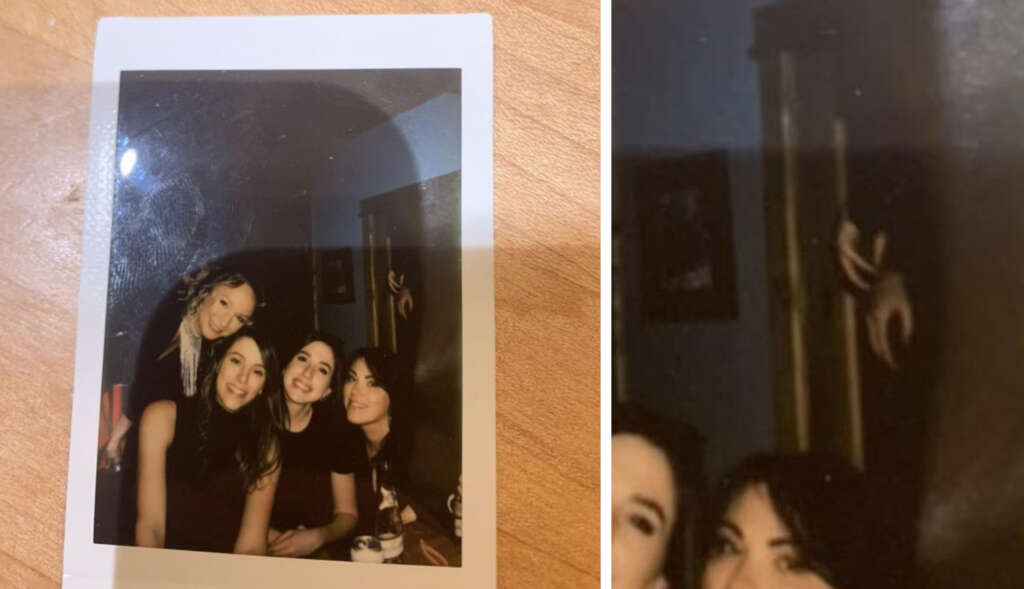 A close-up photo of a Polaroid picture on a wooden surface. The Polaroid shows four women smiling and posing closely together. There is a darkened, blurred figure in the background, partially visible in a suit of armor.