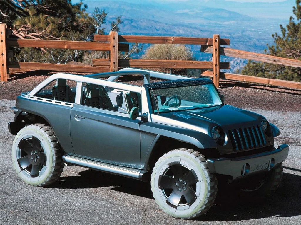 A rugged, open-top SUV with a silver and teal color scheme is parked on a scenic mountain overlook. The vehicle features large tires, a robust design, and distinctive grille, with a wooden fence and vast landscape visible in the background.