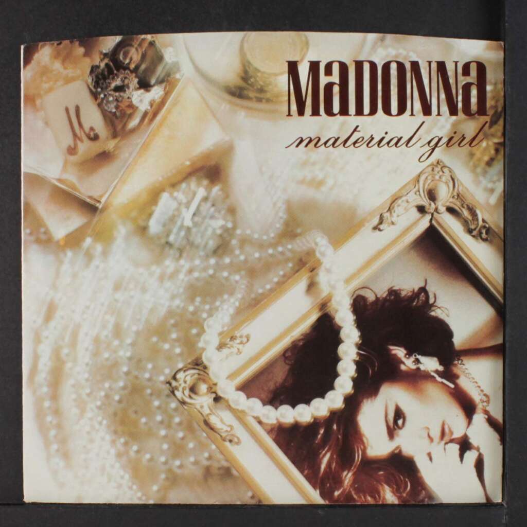 A stylized album cover with "Madonna" and "Material Girl" text. The image features a woman lying down surrounded by luxurious items like pearls, a framed photo, and a large fabric M. The color scheme is warm and golden, evoking a sense of opulence.