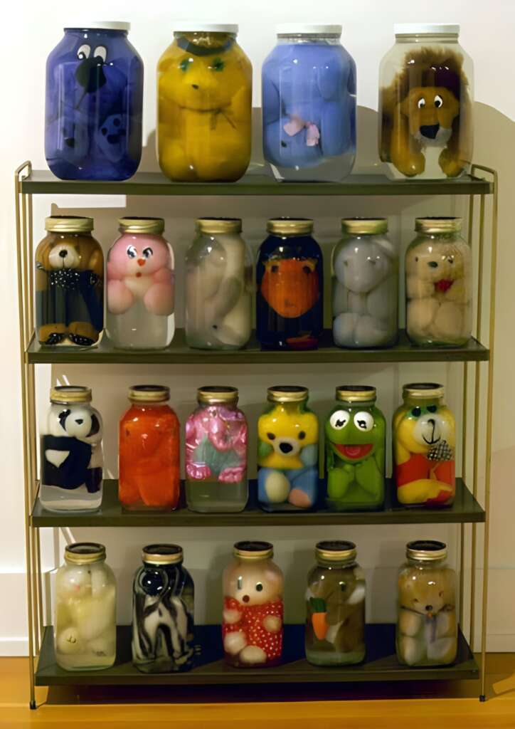 A four-shelf unit displaying jars filled with preserved plush toys, each jar containing a different stuffed animal. The toys include various characters, including a frog, a caterpillar, and others, with some being positioned to face outward for visibility.