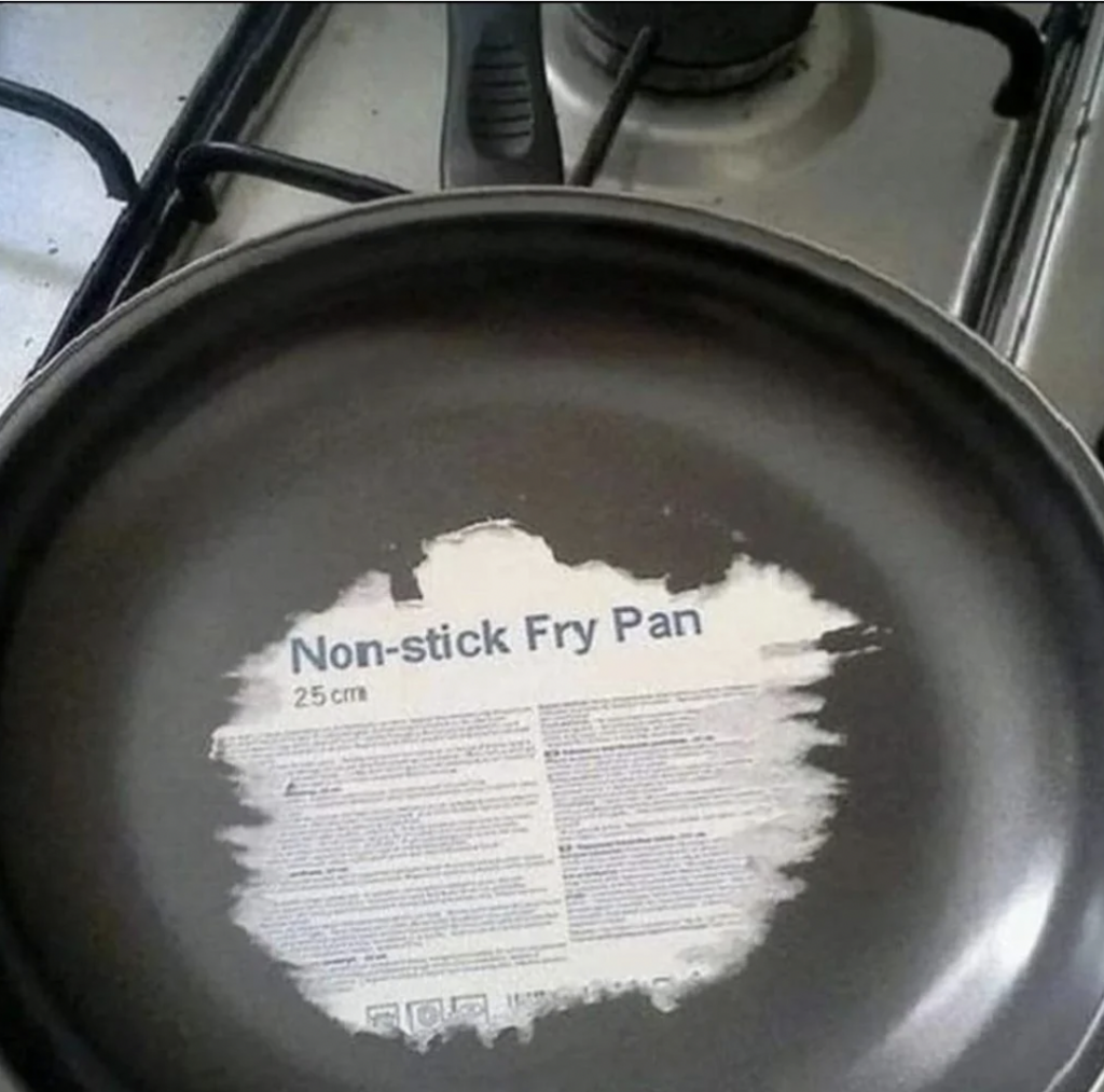 A non-stick frying pan with the label still attached, showing "Non-stick Fry Pan 25 cm." The pan is sitting on a stove with a gas burner visible in the background. The label has not been removed before using the pan.